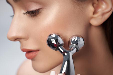 Close up side view portrait of woman massaging her cheek with massage roller