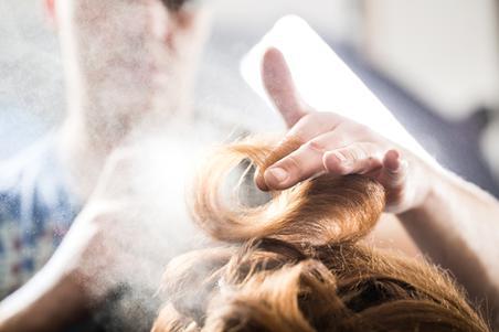 hairdresser styling with hairspray to long curly hair