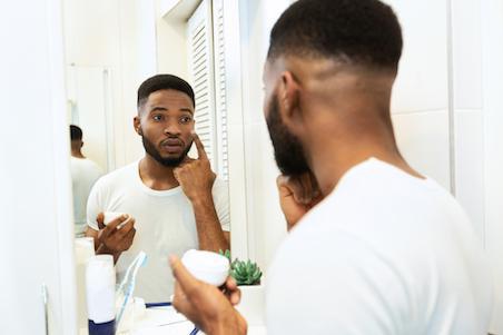 man applying moisturiser in the mirror in a bathroom