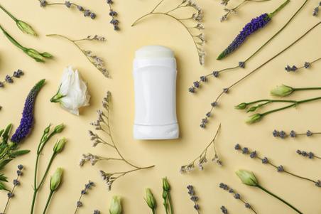 Natural deodorant on yellow background with plants surrounding it