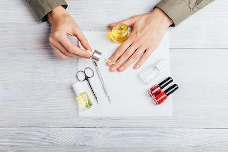 woman applying cuticle oil surrounded by other nail care items