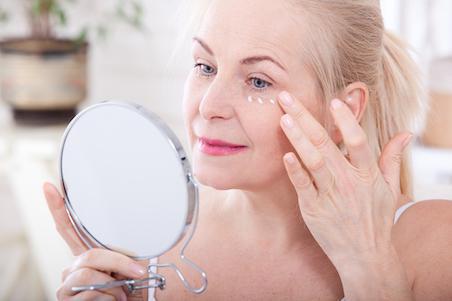 woman applying eye cream in hand mirror