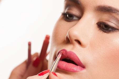 Woman applying pink lipstick with a lip makeup brush