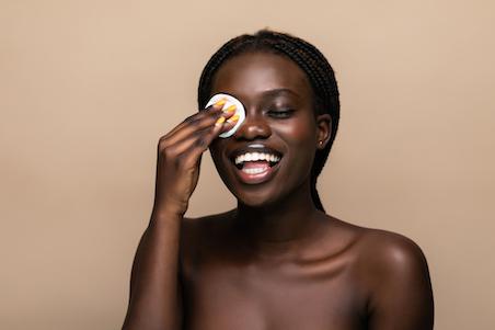 woman smiling and removing eye makeup with a cotton pad
