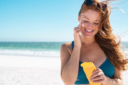 woman smiling applying sunscreen to face