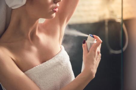 Woman wearing a towel applying spray deodorant