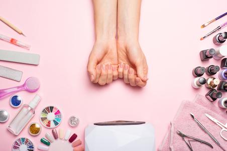 Women's hands near a set of professional manicure tools on a pink background