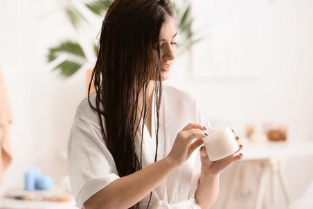Young woman applying cream to long hair in bathroom