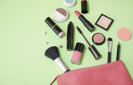 Makeup spilling out of a pink bag on a green background