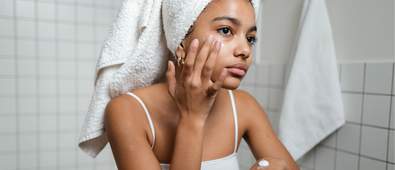 woman putting moisturiser of her face with a towel on her head