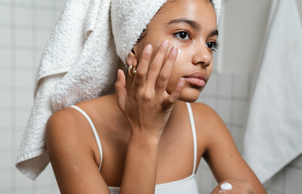 woman putting moisturiser of her face with a towel on her head