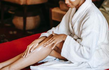 women in white robe moisturising her legs