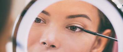 woman applying mascara through mirror