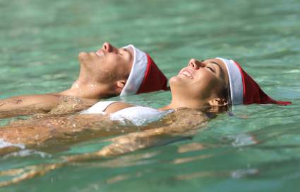 Man and woman floating in a pool wearing Santa hats