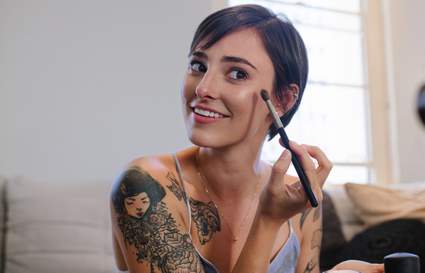 woman with tattoos applying makeup for vlog