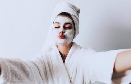 woman taking a selfie with face mask on and dressing gown and towel