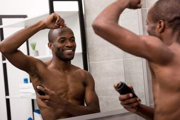 Shirtless man applying antiperspirant spray.